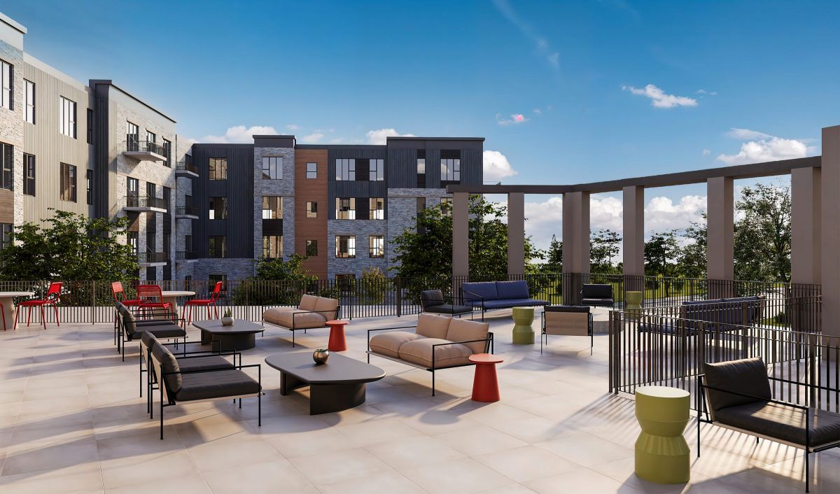 Modern apartment courtyard with outdoor seating, tables, and greenery under a blue sky with scattered clouds at Volta apartments.