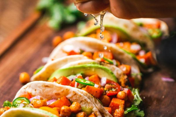 A hand squeezes lime over vegetable-filled tacos on a wooden board, garnished with fresh herbs.